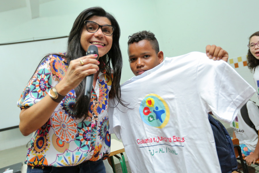 Luzia Rodrigues, coordenadora pedagógica do PCJE, presenteia estudante com camiseta. Foto: Itawi Albuquerque